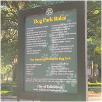 A large green and black sign detailing the "Dog Park Rules" for the City of Tallahassee, likely posted at San Luis Mission Park.